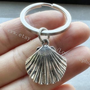 Pode incluir: Chaveiro de prata com um charme de concha de mar de prata. A concha tem um design detalhado e texturizado.