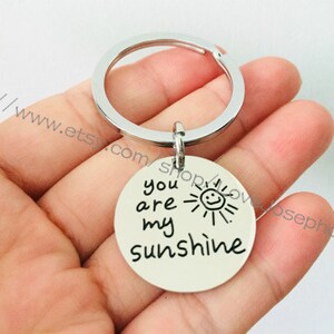 May include: Silver keychain with a round charm that says "You are my sunshine" with a hand-drawn sun with a smiley face.
