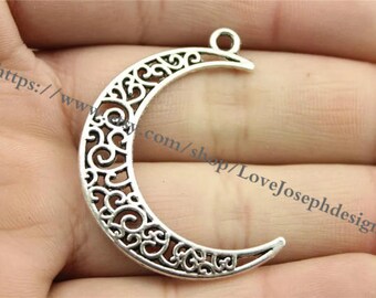May include: Silver-toned crescent moon charm with an intricate filigree design. The charm has a loop at the top for attaching to jewellery or other crafts.