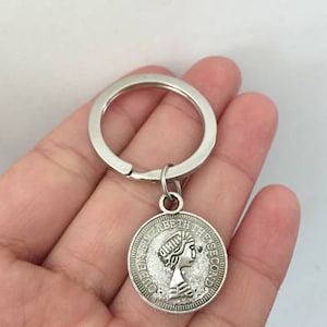 May include: Silver keyring with a round charm featuring a profile of Queen Elizabeth II and the text "Queen Elizabeth The Second".