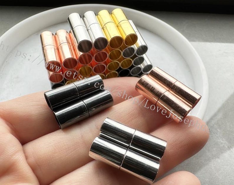 May include: Assortment of magnetic clasps for jewelry making in silver, gold, and rose gold tones. The clasps are arranged in a stack and on a hand.