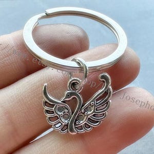 Könnte beinhalten: Silberner Schlüsselanhänger mit einem Schwanen-Anhänger. Der Schwan ist mit filigranen Flügeln und einem zarten Körper verziert.