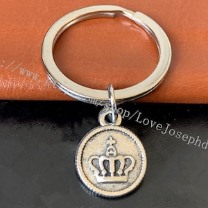 May include: Silver key chain with a crown charm. The crown is detailed with a cross at the top and a decorative design.
