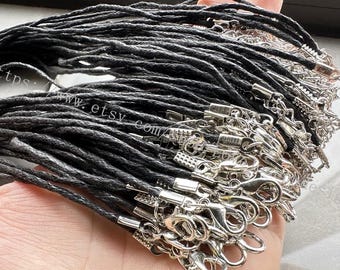 May include: A collection of black cord necklaces with silver-colored lobster claw clasps. The cords are tightly woven, and the clasps are attached to the ends. The image shows a close-up view of the necklaces, highlighting the texture and details.