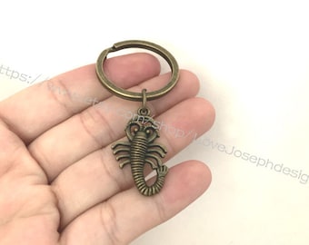 Puede incluir: Un llavero de escorpión de bronce con un anillo redondo. El escorpión está detallado con un cuerpo y patas segmentados.