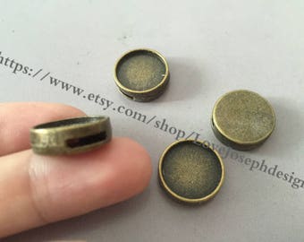 May include: Four antique bronze-colored metal bezel settings. One is held by a finger. The settings are round with a flat surface and a small hole on the side. The Etsy shop URL is visible in the background.