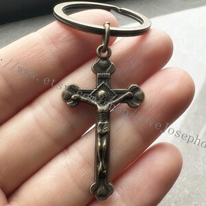 May include: A bronze-colored metal keychain with a crucifix pendant. The crucifix features a detailed depiction of Jesus Christ on the cross.