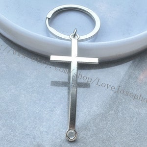 Op de afbeelding: Zilveren kruis sleutelhanger met een zilveren sleutelring. Het kruis is een eenvoudig ontwerp met een afgeronde boven- en onderkant.