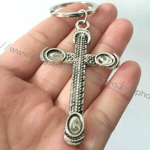 May include: Silver-toned cross keychain with a detailed design. The cross has three circular accents on each side.