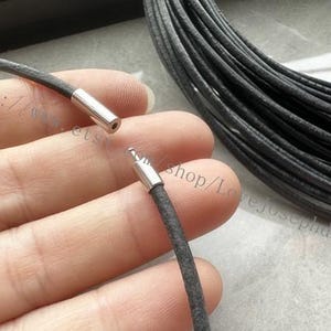 May include: Close-up of a black leather cord with silver metal end caps. The cord is being held in a hand. The cord is approximately 2 mm in diameter.