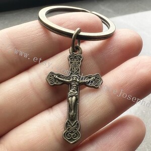 May include: A silver-toned metal cross keychain with a figure of Jesus Christ on the cross. The cross has intricate details and a ring attached to the top.