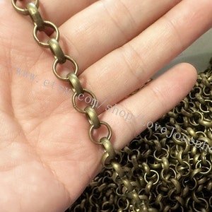 May include: A close-up of a gold-toned chain with round links. The chain is lying on a hand, and the background is blurred.