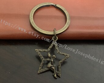 Könnte beinhalten: Ein Schlüsselanhänger aus Bronze mit einem sternförmigen Anhänger, der eine Feensilhouette zeigt. Der Anhänger ist an einem Schlüsselring aus Bronze befestigt.