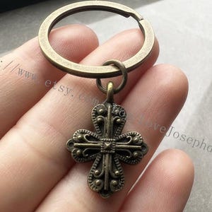 May include: A bronze key chain with a detailed cross charm. The cross has a decorative design with small circles around the edges.