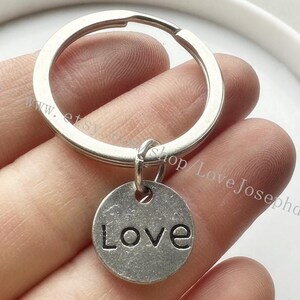 Può includere: Portachiavi d'argento con un ciondolo rotondo che dice "Love".