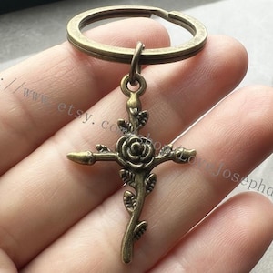 May include: A bronze-colored key chain with a rose-shaped cross charm. The cross is detailed with leaves and a rose in the center.