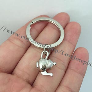 Puede incluir: Llavero de plata con un dije de tetera. La tetera tiene una tapa y un pico.