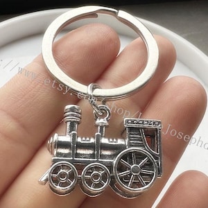Puede incluir: Llavero plateado con un modelo detallado de una locomotora de vapor vintage. El tren tiene un acabado negro y plateado y está unido a un llavero plateado.