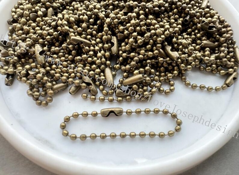 May include: A pile of brass ball chain with a single chain separated for display. The chain is made of small, round, brass beads.