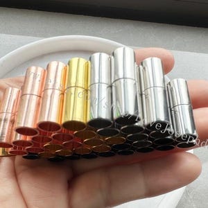 May include: A collection of silver, gold, and rose gold metal end caps for necklaces or bracelets. The caps are cylindrical and have a smooth finish.