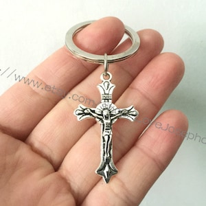 May include: Silver-toned metal keychain featuring a crucifix with a figure of Jesus Christ. The crucifix has a decorative crown at the top and the inscription "INRI" on the crossbar.
