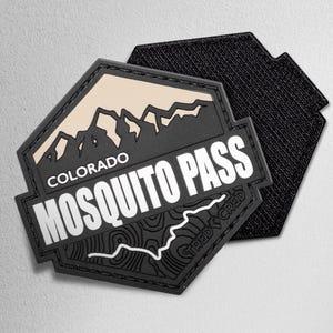 May include: A black and tan hexagonal patch with the text "COLORADO MOSQUITO PASS" and a mountain graphic. The patch has a topographic map design and the text "TRED CRED". The back of the patch is black.