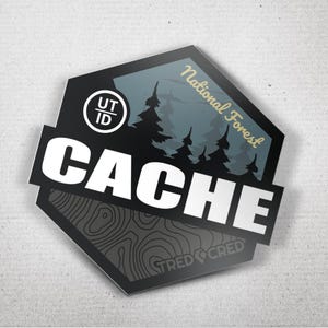 May include: A black and gray sticker with the word "CACHE" in large white letters. The sticker features a forest scene and the text "National Forest" in gold. The bottom of the sticker has the text "TRED CRED".