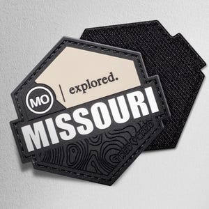 May include: A black and tan patch with the word "MISSOURI" in white block letters. The patch has a topographic map design and the text "explored." The patch also has the letters "MO" in a white circle.