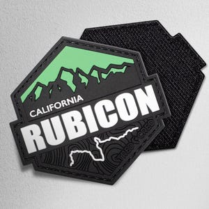 May include: Black and green patch with the word "RUBICON" in white, a mountain graphic, and the text "CALIFORNIA". The patch has a textured border and a hook-and-loop backing.