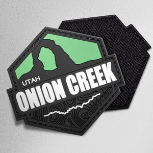May include: A black and green patch with the words "UTAH ONION CREEK" in white. The patch features a green archway design and a topographic map. The patch has a hook and loop backing.