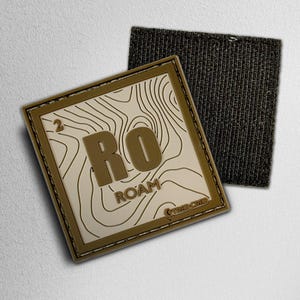 May include: Square patch with a topographic map design in tan and brown, featuring the letters "RO" and the word "ROAM". The patch has a textured border and a hook-and-loop backing for attachment.