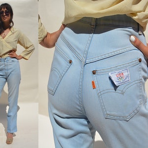May include: Light blue high-waisted jeans with a small patch on the back pocket that reads "1984 USA Olympic Games".