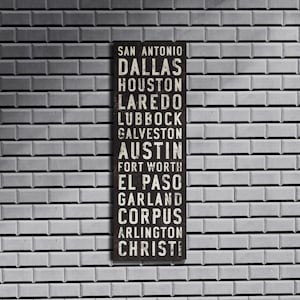 May include: A black and white sign with the names of Texas cities printed in white. The cities listed are San Antonio, Dallas, Houston, Laredo, Lubbock, Galveston, Austin, Fort Worth, El Paso, Garland, Corpus, Arlington, and Christi.