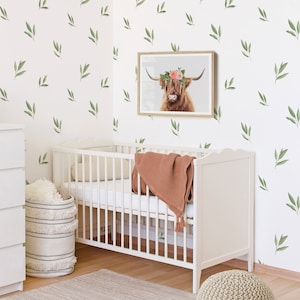 May include: A white crib with a brown blanket and a white wicker basket with a white and black striped pattern. The crib is in a room with white walls and a floral wallpaper pattern. A framed print of a Highland cow with a floral crown is hanging on the wall.