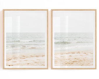 May include: Two framed prints featuring a beach scene. The images depict a sandy beach with gentle waves and a calm ocean under a pale sky. The frames are made of light-colored wood, adding a natural touch to the coastal theme.