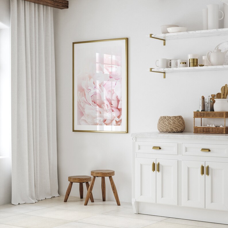 Pu&ograve; includere: Una cucina bianca con una stampa di peonia rosa incorniciata in oro, due sgabelli in legno e un armadio bianco con ferramenta dorata.