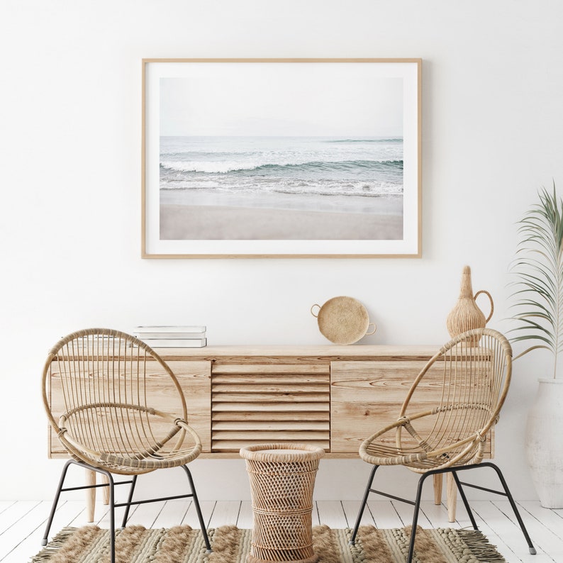 May include: A living room interior with two wicker chairs, a wooden cabinet, a woven tray, and a woven basket. A framed photograph of a beach scene with waves crashing on the shore hangs on the wall.