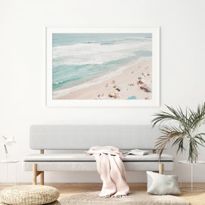 May include: An aerial photograph of a beach with turquoise water and white sand.  People are scattered across the beach, enjoying the sun and relaxing under colorful umbrellas.