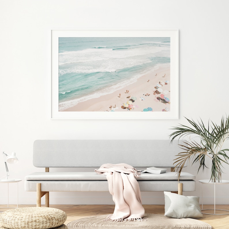 May include: An aerial photograph of a beach with turquoise water and white sand.  People are scattered across the beach, enjoying the sun and relaxing under colorful umbrellas.