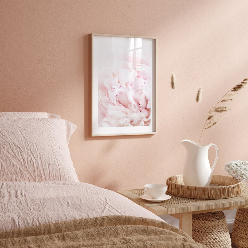 Pu&ograve; includere: Una stampa incorniciata di un primo piano di un fiore di peonia rosa. La stampa &egrave; appesa a una parete rosa chiaro in una camera da letto.