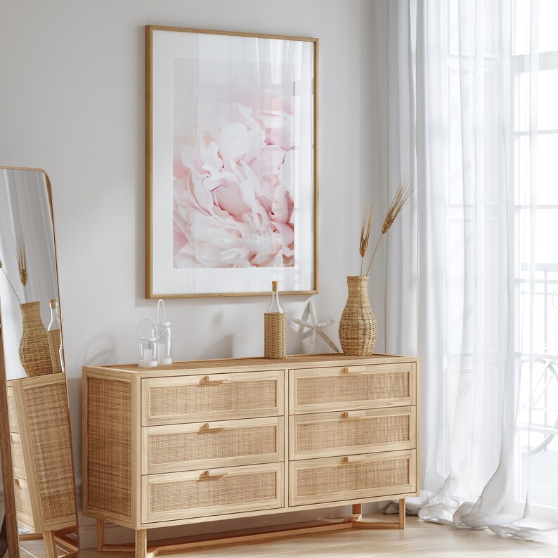 Pu&ograve; includere: Una cassettiera in legno chiaro con sei cassetti, ognuno con un frontale in rattan intrecciato. La cassettiera ha una cornice in legno chiaro e poggia su gambe inclinate. Una stampa incorniciata di un fiore di peonia rosa &egrave; appesa al muro sopra la cassettiera. Un vaso con steli di grano secco e una bottiglia di vetro trasparente con un tappo di sughero sono sulla cassettiera.