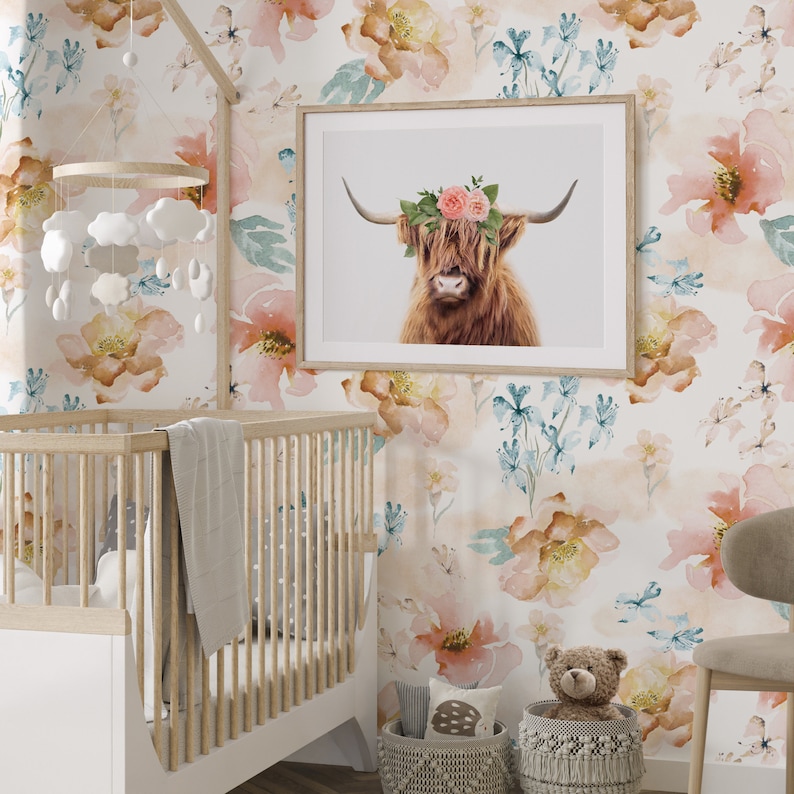 May include: A nursery room with a white crib, a floral wallpaper with pink and brown flowers, a framed print of a Highland cow with a flower crown, a wicker basket with a stuffed animal, and a white wicker basket with a stuffed animal.