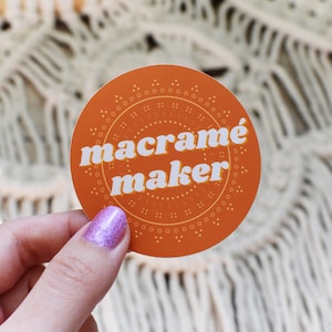 May include: A round orange sticker with a white border and the text "macramé maker" in white letters.