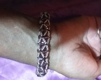 Puede incluir: Un primer plano de un brazalete de cuentas con cuentas negras y moradas dispuestas en un patrón geométrico.