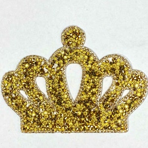 May include: A gold crown-shaped embellishment made of rhinestones. The crown is a decorative patch that can be ironed onto fabric.