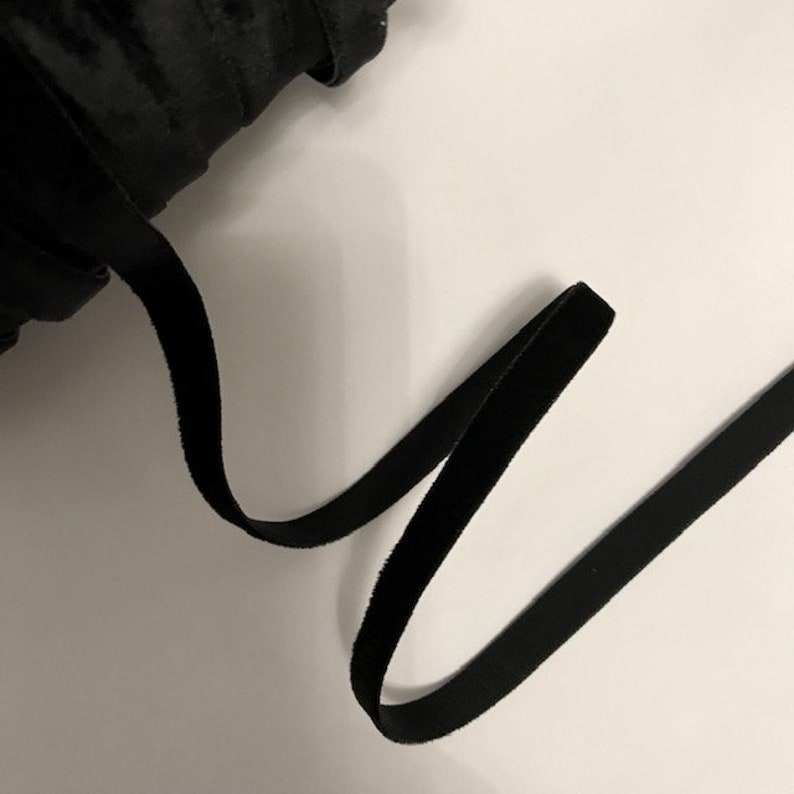 Pu&ograve; includere: Un primo piano di un nastro di velluto nero. Il nastro &egrave; arrotolato e una sezione &egrave; srotolata, mostrando la morbida texture del tessuto.