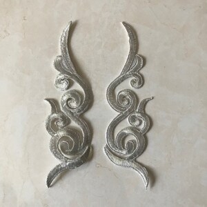 Puede incluir: Dos apliques de tela decorativos de color plateado con un diseño floral en espiral. Los apliques son perfectos para agregar un toque de elegancia a la ropa, las manualidades o la decoración del hogar.