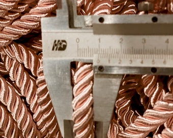 May include: Close-up of a pink braided cord measured with a ruler. The cord is approximately 1/2 inch wide.