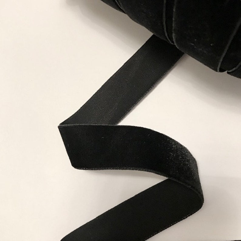 Pu&ograve; includere: Nastro di velluto nero, un tessuto morbido e lussuoso, mostrato in un'immagine ravvicinata. Il nastro &egrave; piegato e curvato, mettendo in evidenza la sua texture liscia e il suo ricco colore.