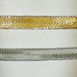 Pode incluir: Duas fitas decorativas com contas. Uma é dourada, com um padrão de chevron e pequenas contas. A outra é prateada, também com um design de chevron. Ambas as fitas têm uma aparência delicada, para artesanato.